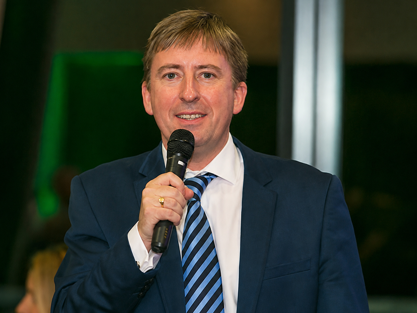 Nick Johnson holding a microphone while hosting an event in a navy suit